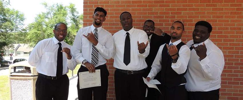 A group of male students holding up their pinky rings.